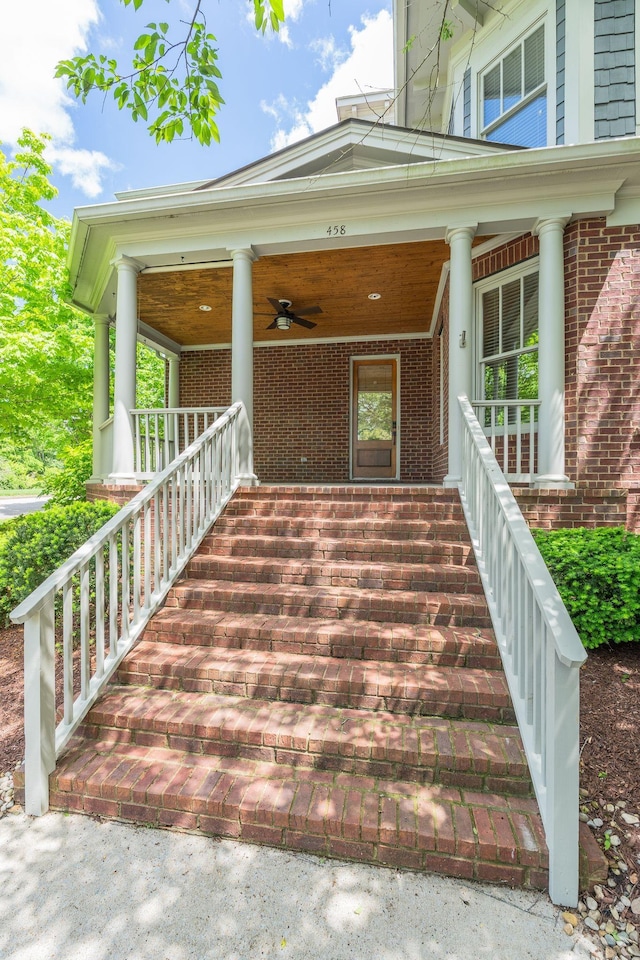 doorway to property featuring covered porch, brick siding, and a ceiling fan