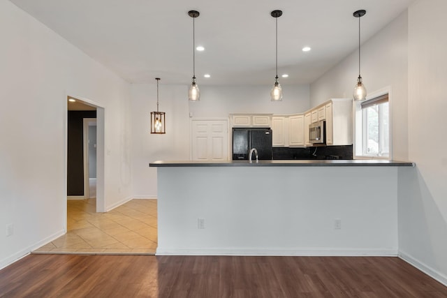 kitchen featuring stainless steel microwave, black fridge, wood finished floors, pendant lighting, and a peninsula