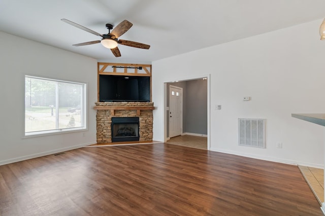 unfurnished living room featuring a ceiling fan, wood finished floors, a stone fireplace, and baseboards