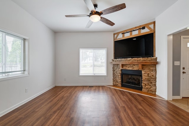 unfurnished living room with wood finished floors, a ceiling fan, baseboards, and a stone fireplace
