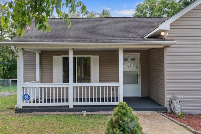 property entrance with a porch, a shingled roof, and fence