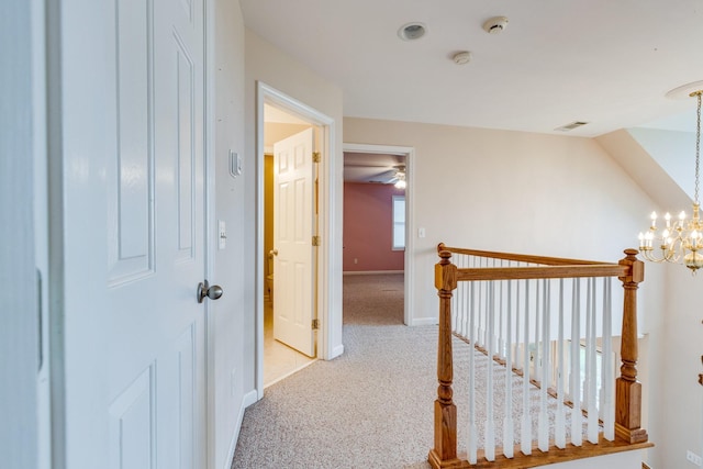 corridor with carpet flooring, a chandelier, baseboards, and an upstairs landing