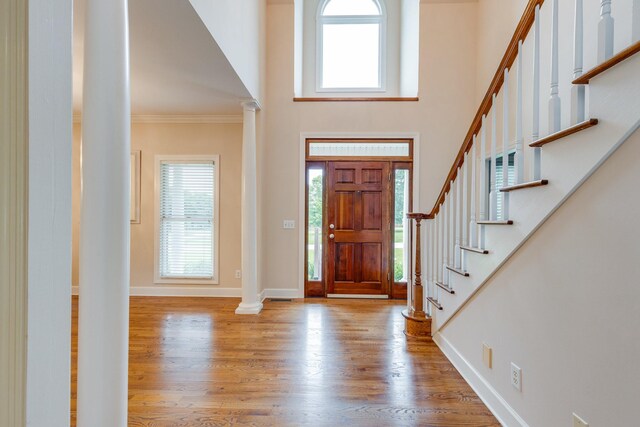 entrance foyer featuring wood finished floors, ornate columns, stairs, a high ceiling, and healthy amount of natural light