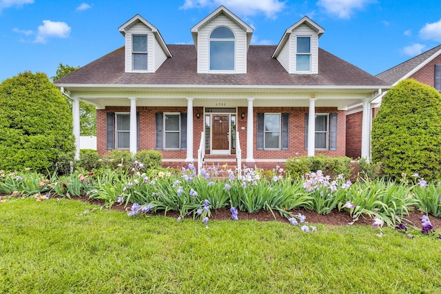 cape cod-style house with brick siding, a front yard, a porch, and a shingled roof
