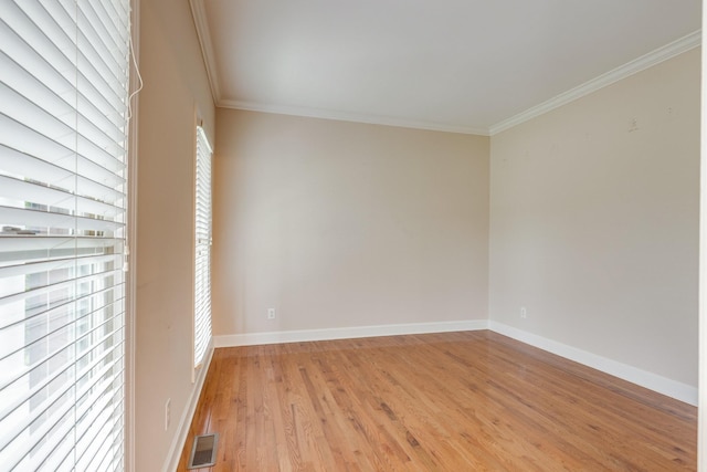 empty room with crown molding, light wood finished floors, and baseboards