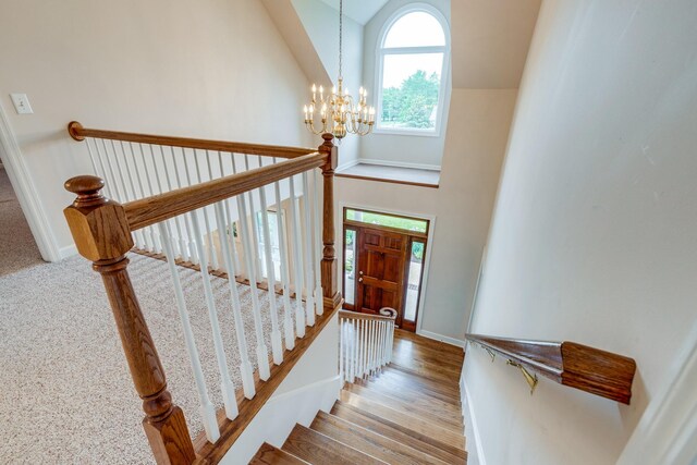 staircase featuring a chandelier, lofted ceiling, baseboards, and wood finished floors