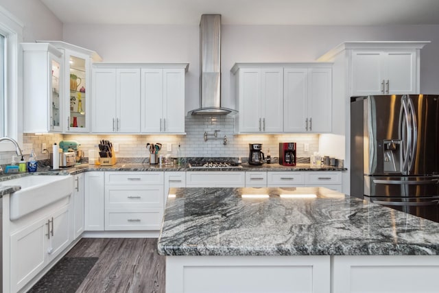 kitchen with stainless steel appliances, wall chimney exhaust hood, white cabinets, glass insert cabinets, and a sink