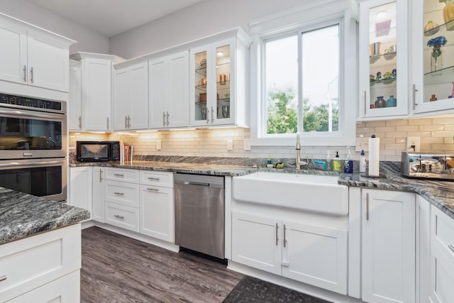 kitchen with stainless steel appliances, a sink, white cabinets, decorative backsplash, and dark wood finished floors