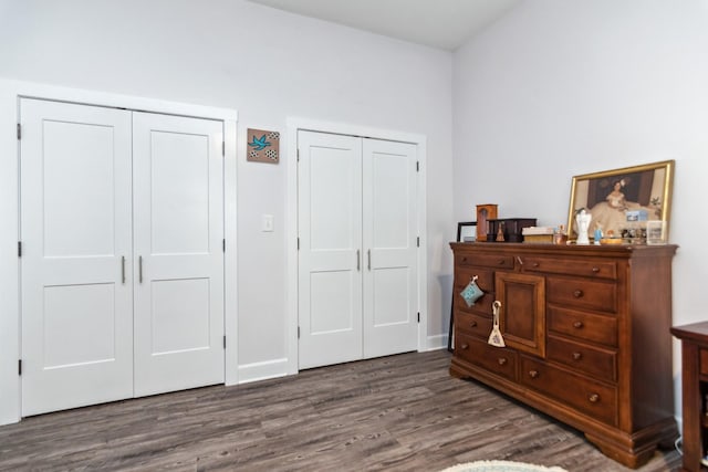 bedroom with two closets, wood finished floors, and baseboards
