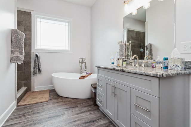 full bathroom with a tile shower, wood finished floors, vanity, a freestanding tub, and baseboards