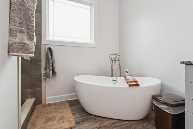 bathroom with wood finished floors, a freestanding bath, and baseboards