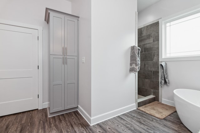 bathroom with a walk in shower, a soaking tub, wood finished floors, and baseboards