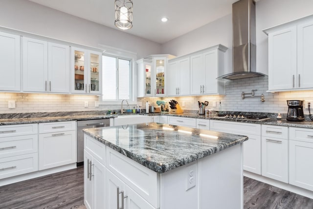 kitchen with wall chimney exhaust hood, appliances with stainless steel finishes, a center island, white cabinets, and dark wood-style flooring