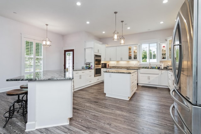 kitchen featuring appliances with stainless steel finishes, a peninsula, glass insert cabinets, tasteful backsplash, and a center island