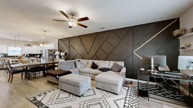 living room featuring ceiling fan, a decorative wall, light wood finished floors, an office area, and a chandelier