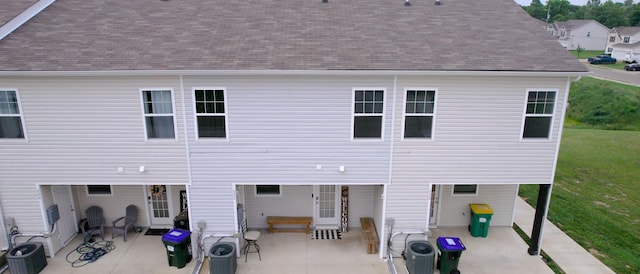 rear view of house with a patio, cooling unit, a shingled roof, and a lawn