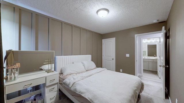bedroom with a textured ceiling, light carpet, baseboards, and connected bathroom