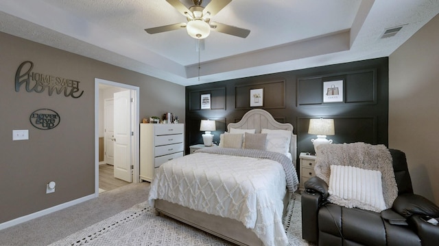 bedroom featuring baseboards, a raised ceiling, light colored carpet, a ceiling fan, and ensuite bath