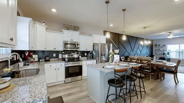 kitchen featuring stainless steel appliances, a sink, light wood-style floors, a kitchen island, and ceiling fan