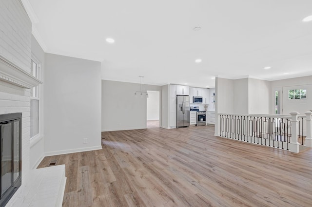 unfurnished living room featuring ornamental molding, light wood finished floors, a fireplace, baseboards, and recessed lighting