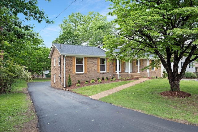 single story home featuring brick siding, asphalt driveway, a front lawn, a porch, and roof with shingles