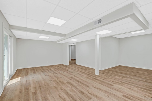 below grade area with light wood-style flooring, a paneled ceiling, baseboards, and plenty of natural light