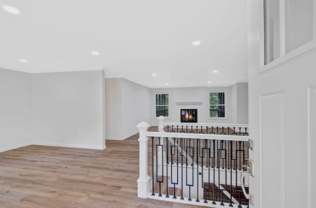 hallway with wood finished floors, baseboards, ornamental molding, recessed lighting, and an upstairs landing