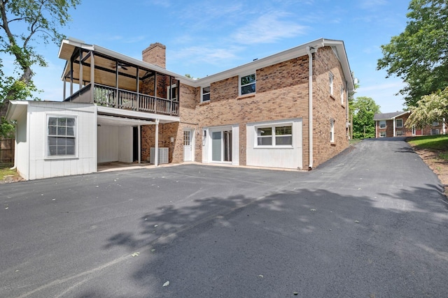 back of house with a chimney, central AC unit, a balcony, and asphalt driveway