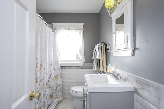 full bathroom with tile walls, toilet, vanity, a wainscoted wall, and tile patterned floors