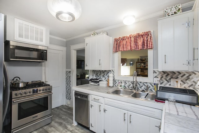 kitchen featuring stainless steel appliances, a sink, light countertops, decorative backsplash, and crown molding