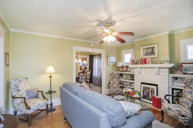 living area featuring wood finished floors, a glass covered fireplace, ceiling fan, baseboards, and crown molding