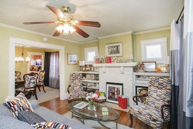 living room with healthy amount of natural light, wood finished floors, a chandelier, crown molding, and ceiling fan