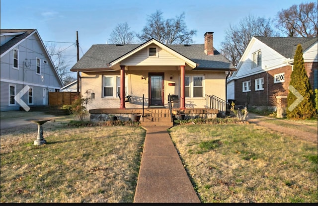 bungalow with covered porch, a front lawn, a chimney, and a shingled roof