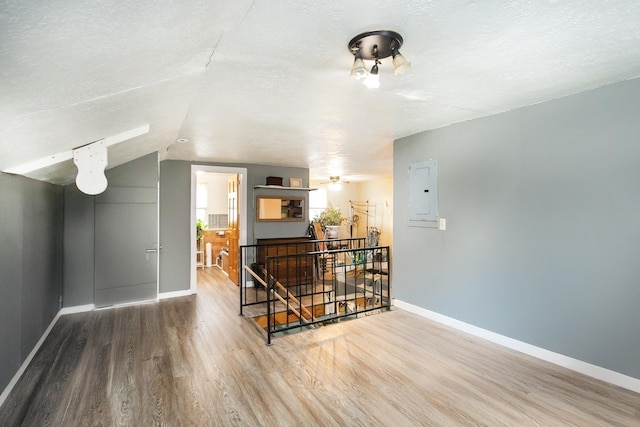 additional living space featuring wood finished floors, baseboards, electric panel, lofted ceiling, and a textured ceiling