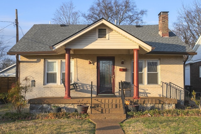 bungalow-style home featuring a porch, brick siding, and roof with shingles
