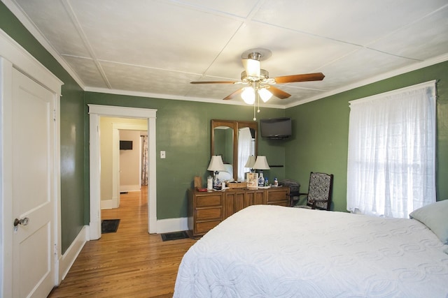 bedroom featuring baseboards, wood finished floors, crown molding, and a ceiling fan