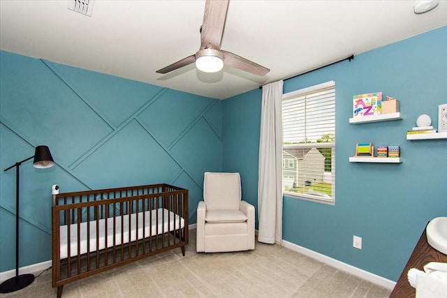 carpeted bedroom featuring baseboards, a crib, and ceiling fan