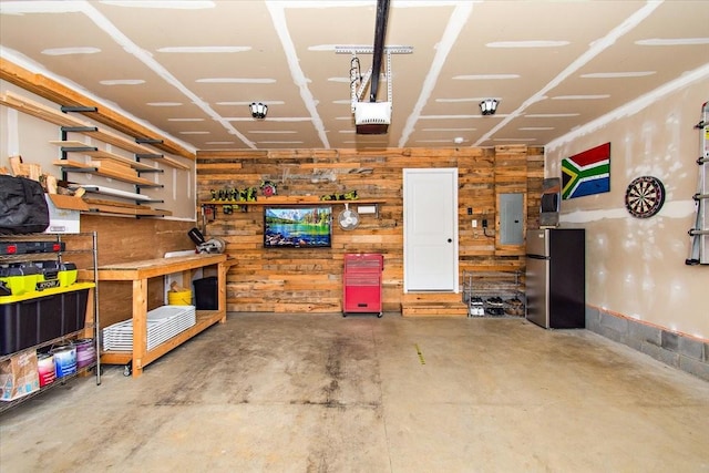 garage featuring freestanding refrigerator, electric panel, wooden walls, and a workshop area