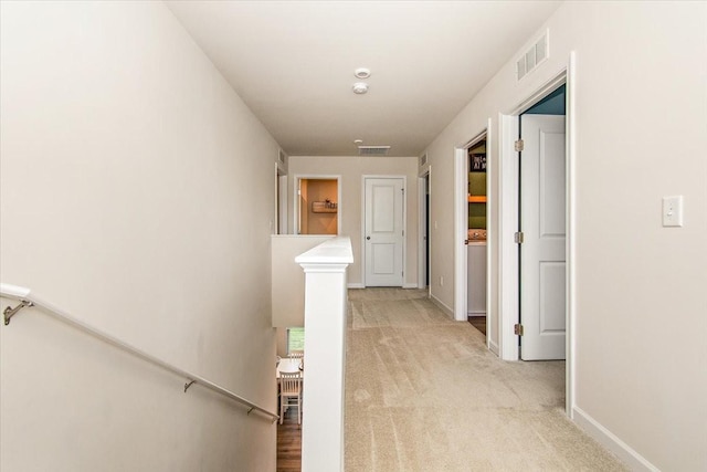 corridor with an upstairs landing, light carpet, and baseboards