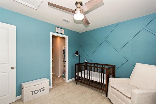 bedroom with carpet floors, a walk in closet, ceiling fan, a crib, and baseboards