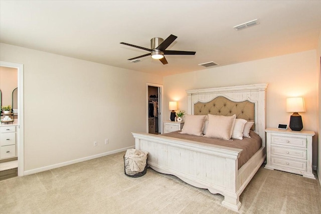 bedroom featuring light colored carpet, a spacious closet, baseboards, and a ceiling fan