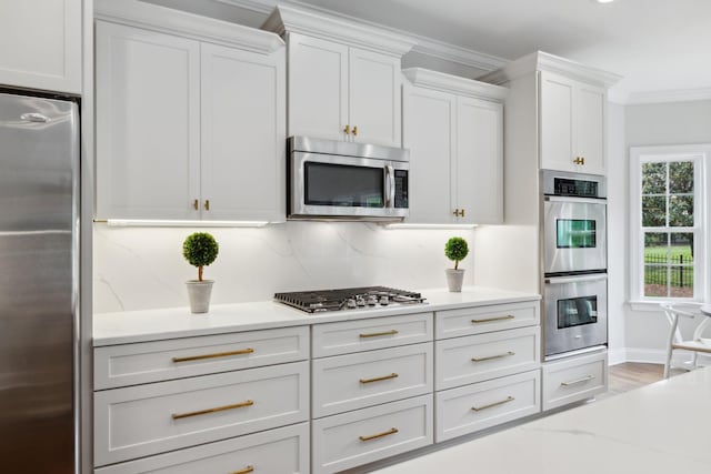 336 Alfred Ladd Rd E, Franklin, TN 37064 - kitchen featuring appliances with stainless steel finishes, ornamental molding, white cabinets, light wood finished floors, and light stone counters
