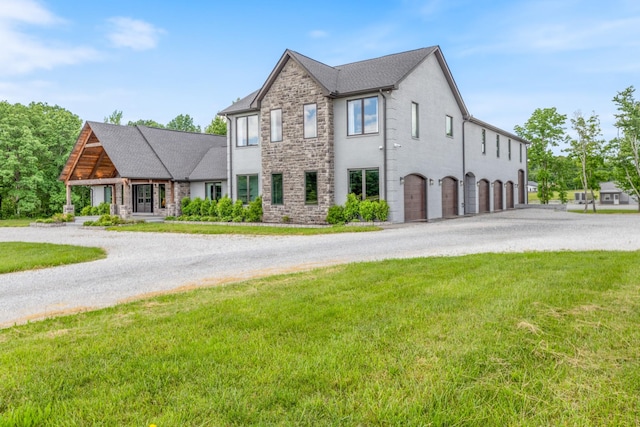 view of front of property featuring curved driveway, stone siding, an attached garage, and a front yard