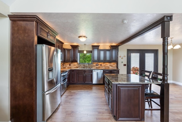 kitchen featuring stainless steel appliances, a sink, a breakfast bar, dark brown cabinetry, and backsplash