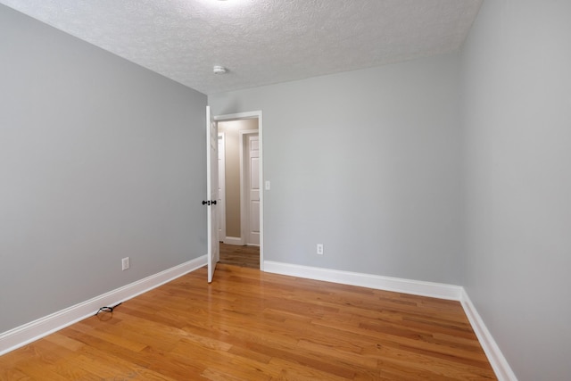 empty room featuring light wood-type flooring, a textured ceiling, and baseboards