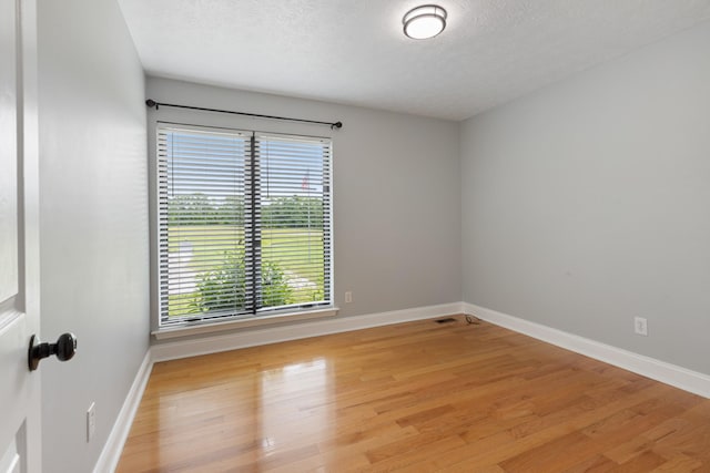 empty room with light wood-type flooring, baseboards, and a textured ceiling