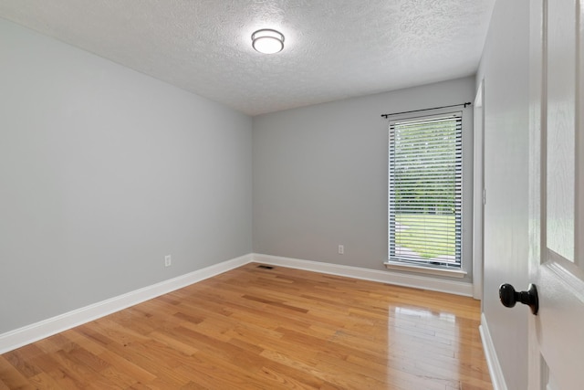 empty room with plenty of natural light, light wood finished floors, baseboards, and a textured ceiling