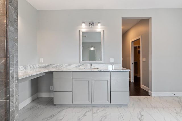 bathroom with marble look tile flooring, baseboards, vanity, and a spacious closet