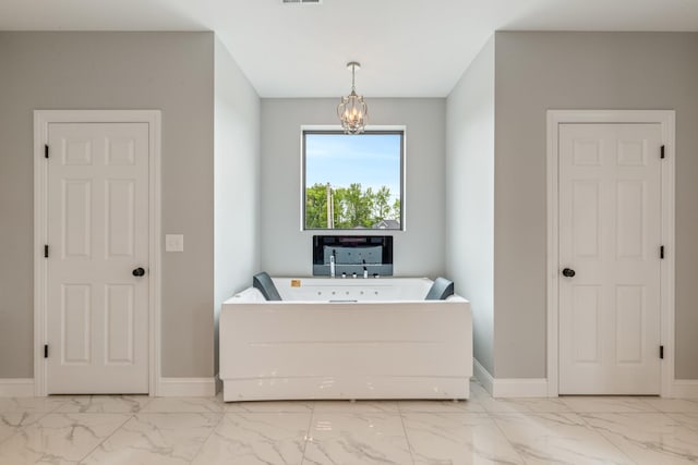 bathroom with marble look tile flooring, a bathtub, a chandelier, and baseboards