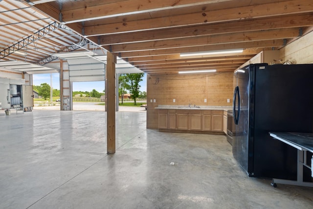 garage featuring freestanding refrigerator, wood walls, and a sink